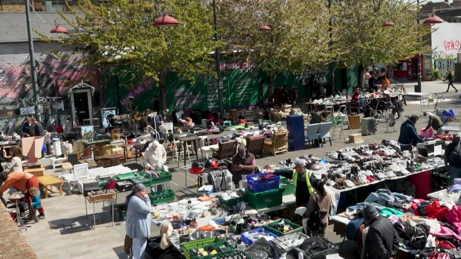 An aerial view of a market, with traders standing behind tables, talking to customers.