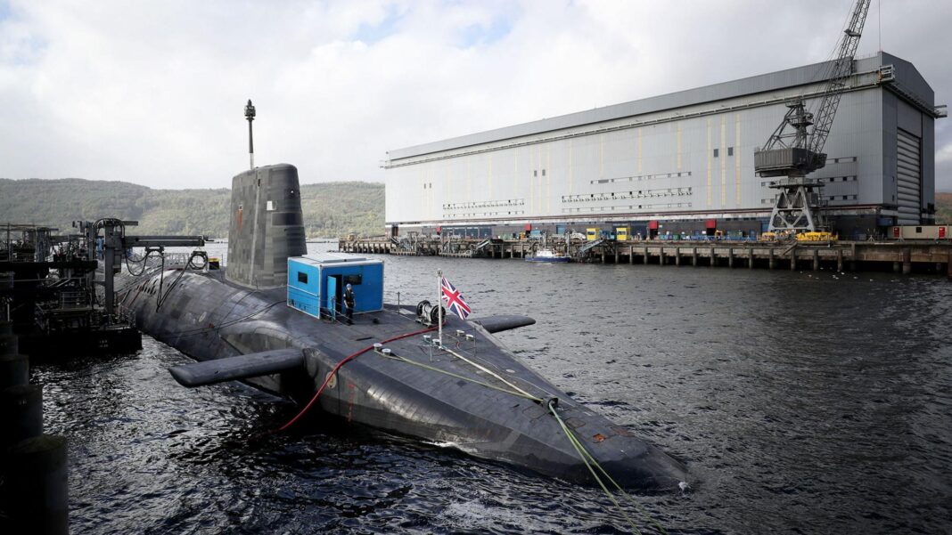 Royal Navy’s new attack submarine arrives at Faslane A submarine with a union flag flying from it, with a large white maintenance building in the background