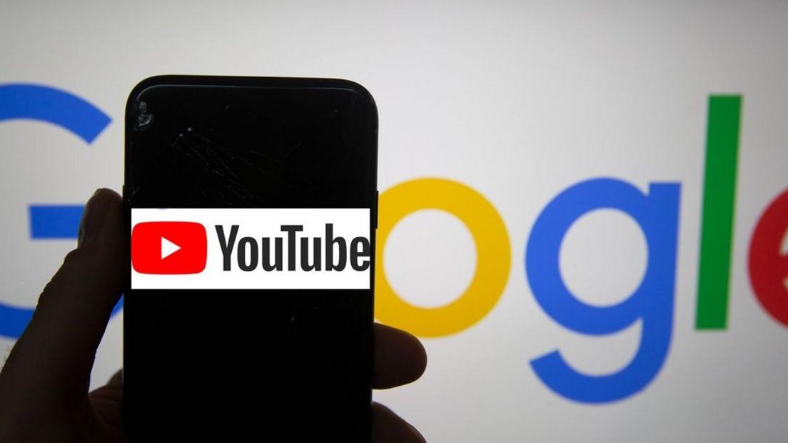 An anonymous hand holding a phone showing YouTube, in front of a Google backdrop