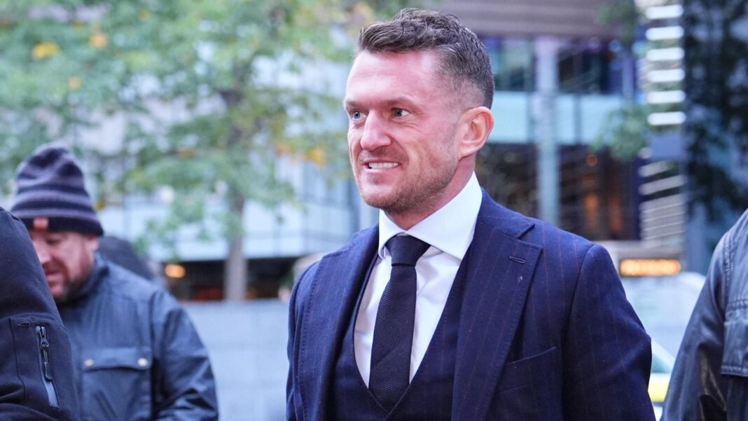 Trial hears Tommy Robinson hired private detectives Tommy Robinson as he walks to court. He is smiling, with a slight grimace, and wears a navy blue pinstriped tie, waistcoat and jacket and white shirt.