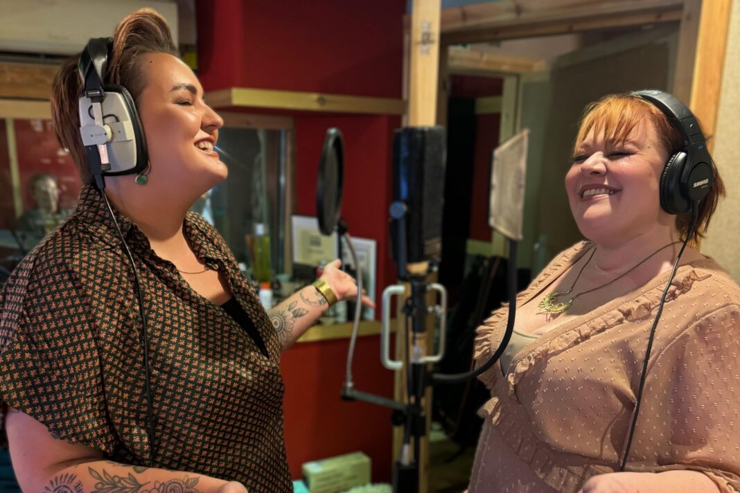 Dolly Parton sings Jolene in Welsh in recording released after her death Two women singing in a studio. There is a mic in front of them and they have headphones on.