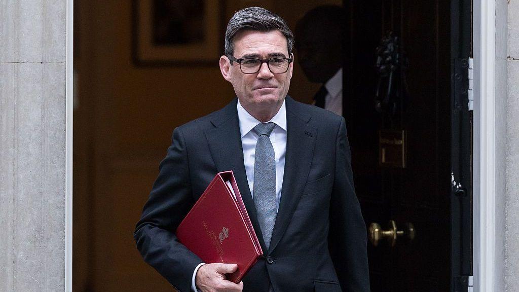 Andy Burnham walks out of Downing Street's black door with a red folder in hand.