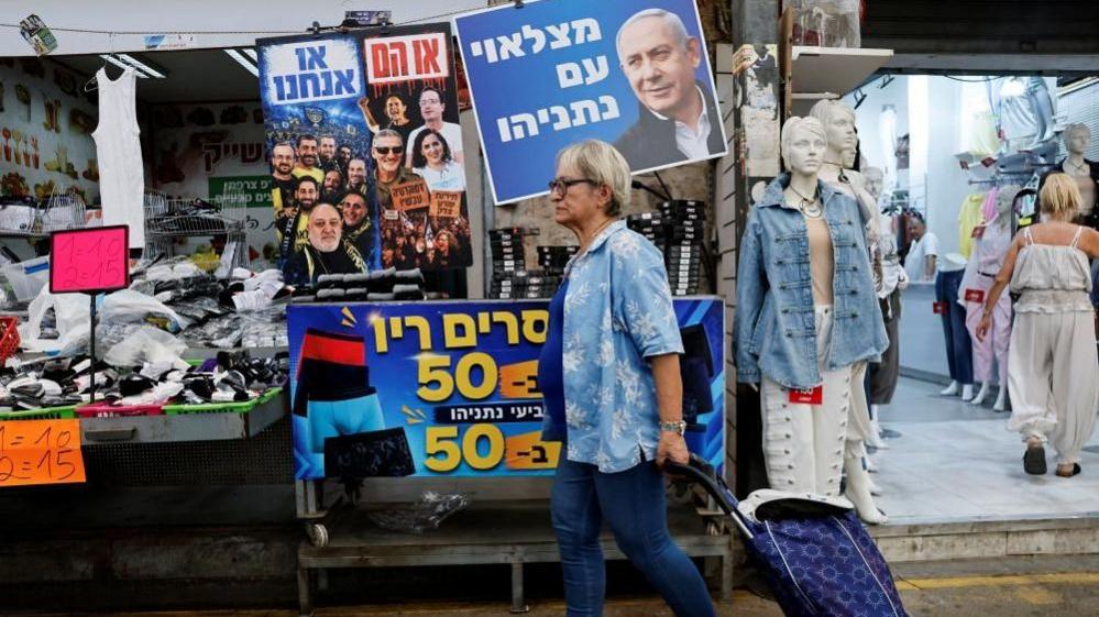 A woman walks past a sign featuring an image of Israeli Prime Minister Benjamin Netanyahu at a market