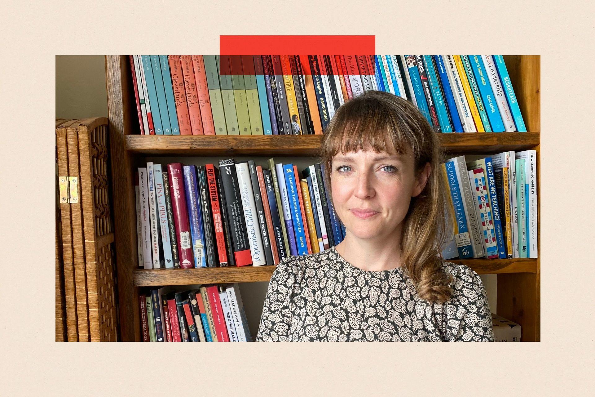 Lucy Crehan stands against a bookcase. She has long brown hair and is wearing a patterned top