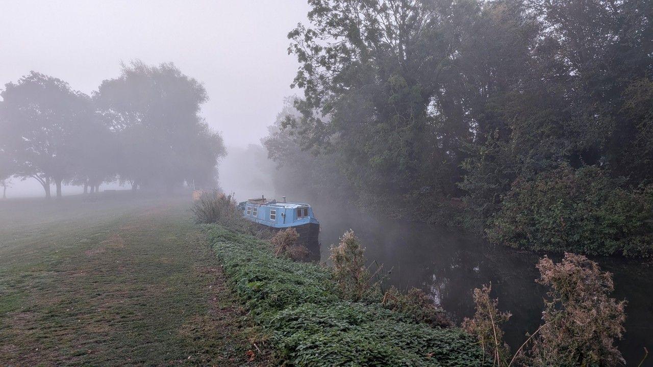 Blue barge on the canal with mist in the background and green shrubbery flanking both banks