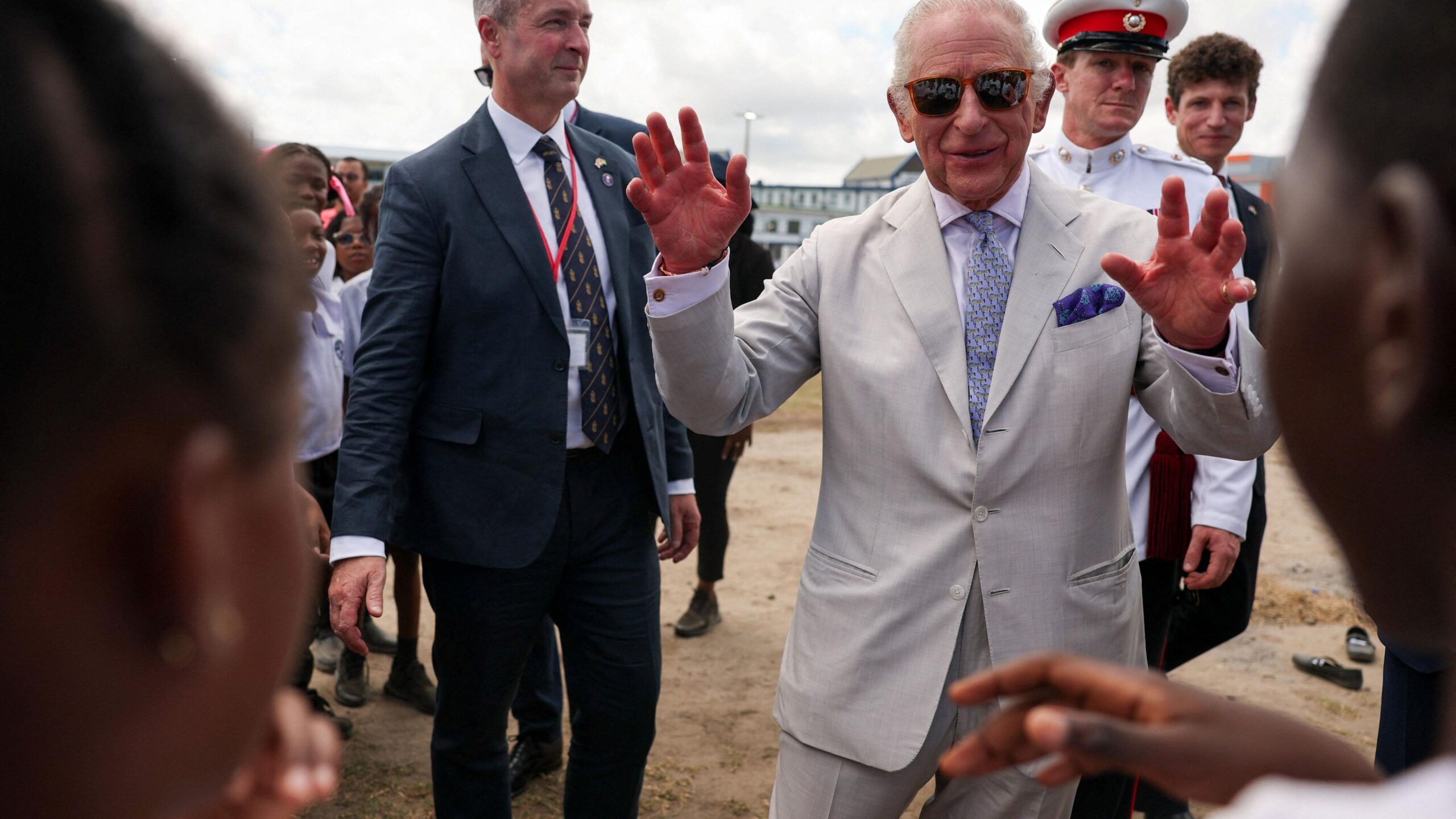 King Charles smiles and waves at young people in a public park