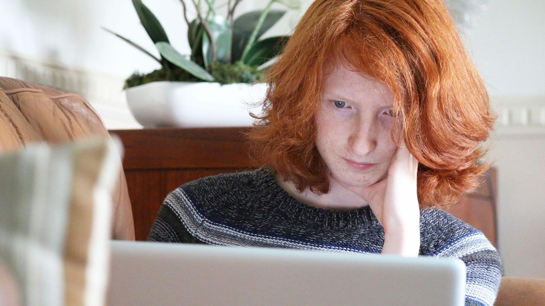 A young woman with red hair looking at a laptop with a serious and thoughtful  expression