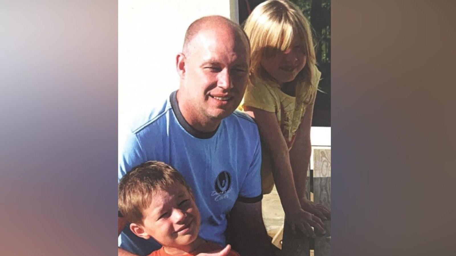 Michael Mullins is pictured next to his two young children. All three are smiling at the camera.