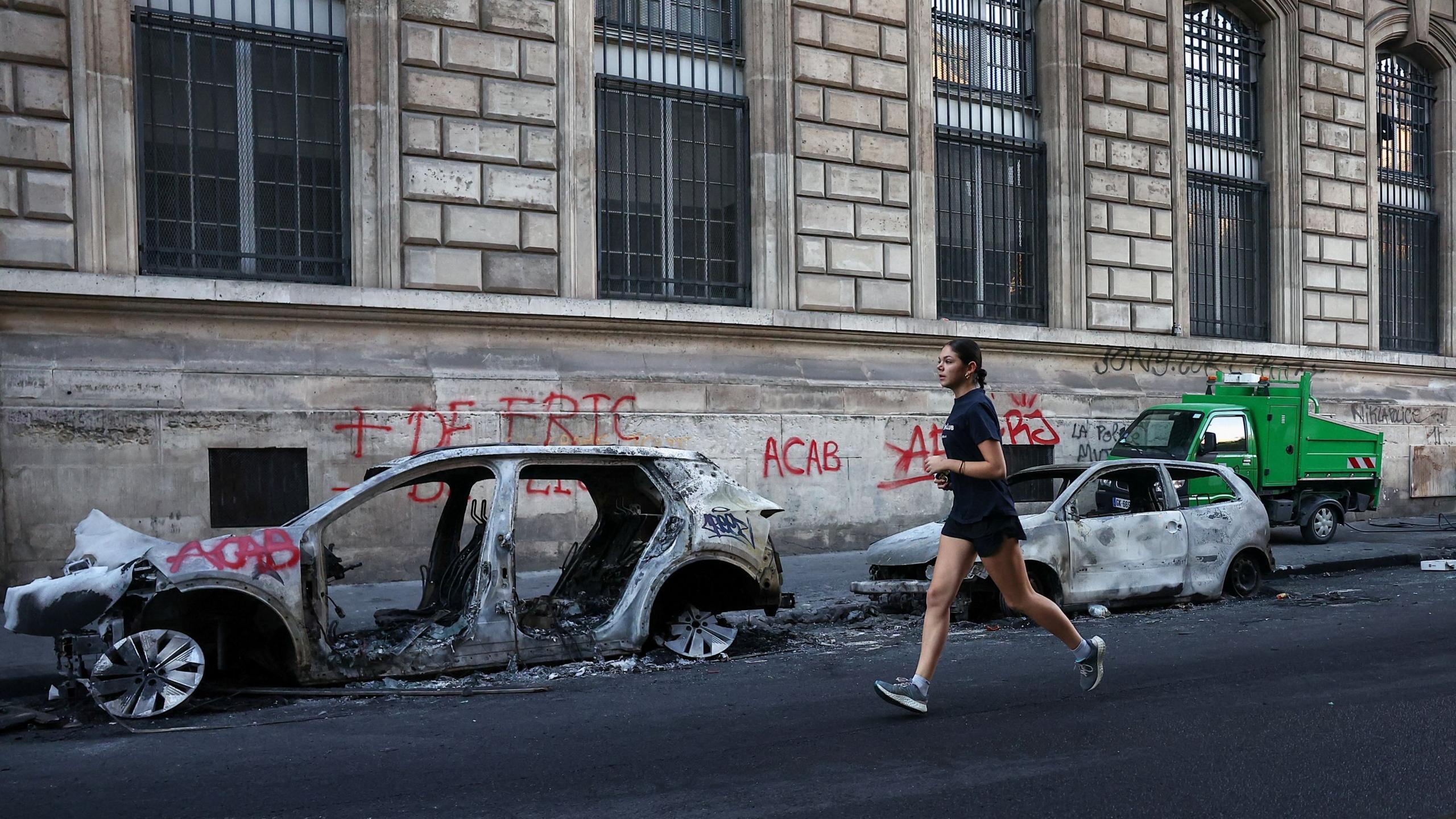 A woman jogs past burnt out vehicles on a street, the day after clashes during a national day of demonstrations against the cost of living and rising fuel prices, near the Place de la Republique in Paris, France, October 18, 2026.