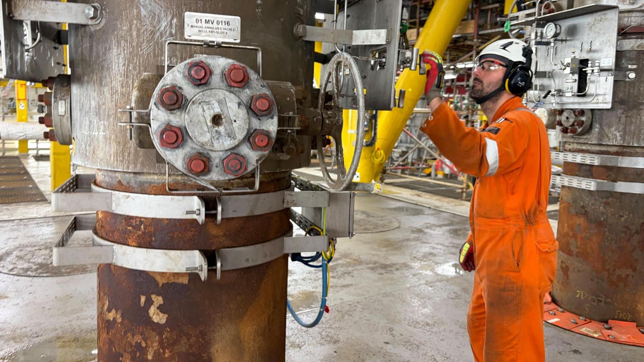 A worker in an orange boiler suit, wearing goggles and a white hard hat, on the Jackdaw platform.