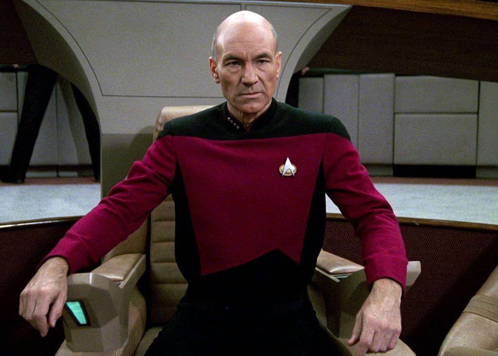 Sir Patrick Stewart seen playing Captain Jean-Luc Picard. He is wearing a red and black Star Trek uniform