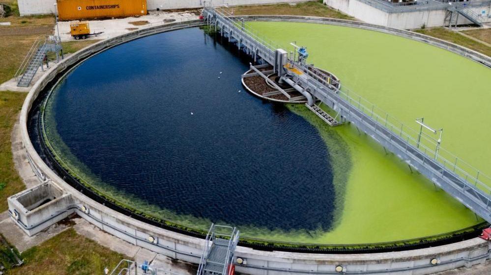 Overhead shot of a sewage treatment works, part of which is covered in what appears to be green algae.