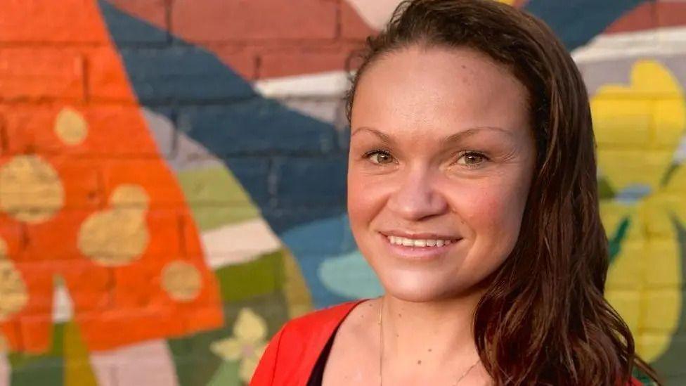 Close up image of Bella Sankey, Leader of Brighton and Hove City Council against a painted wall.