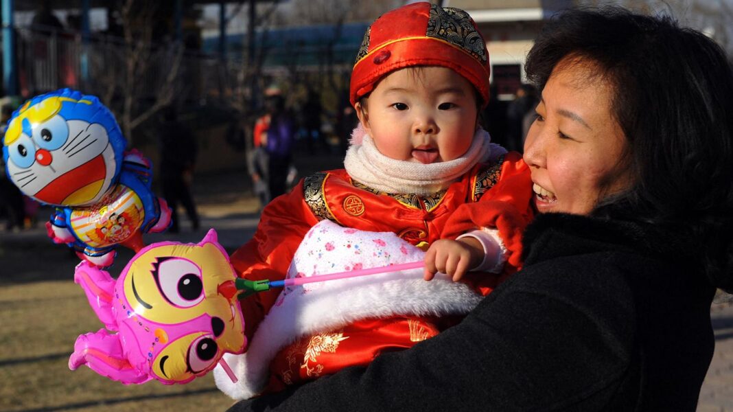 China’s families are now supporting more old people than kids A Chinese woman is outside. She is laughing and holds a baby girl wearing traditional Chinese dress who she is looking at. The baby is holding a balloon