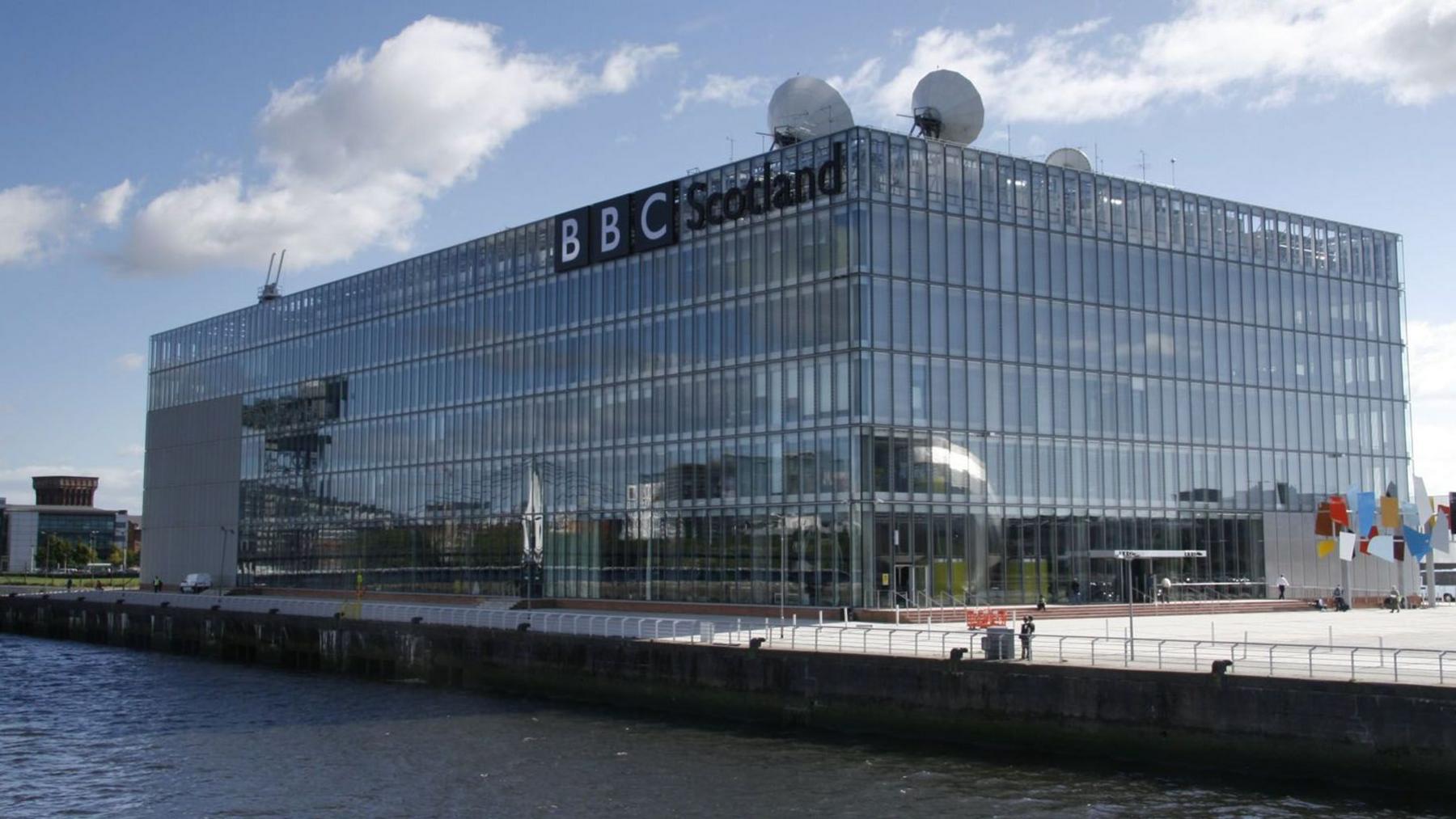 A large square windowed building with a large sign saying 'BBC Scotland' it. It has antennas coming from the top.