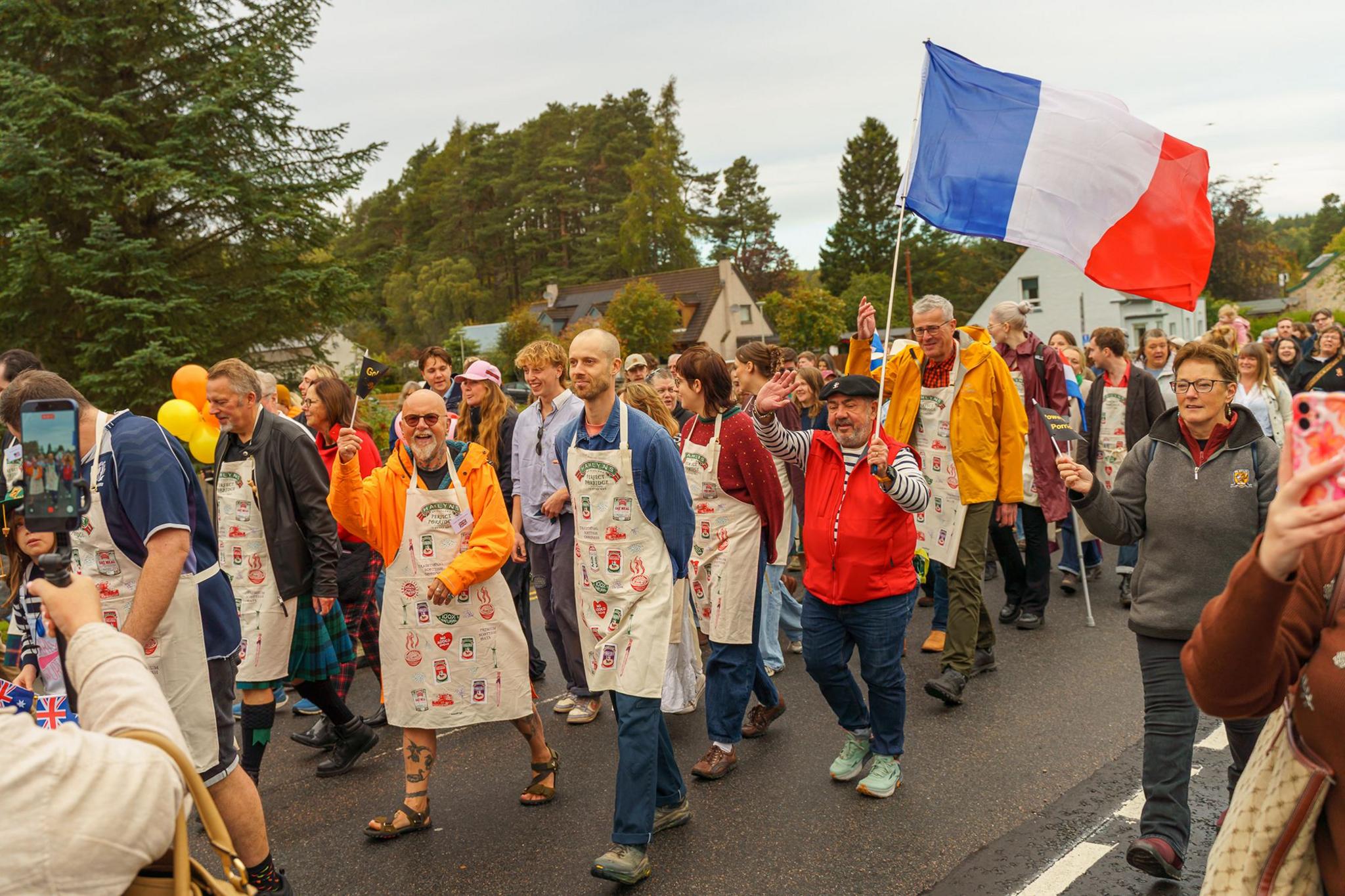 A group of people in aprons in a procession, one of them holding a French flag