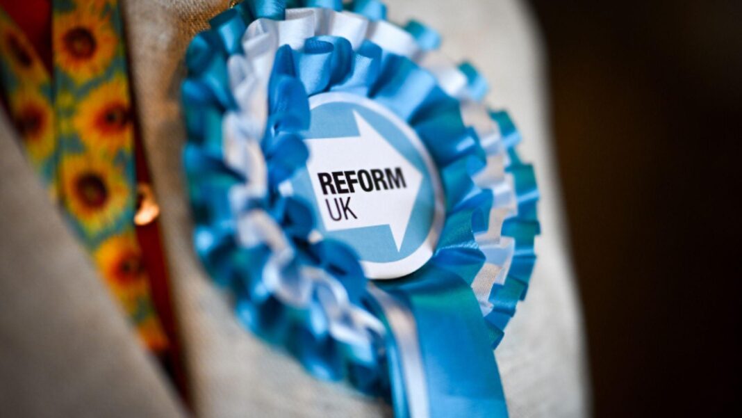 Farage vows to scrap tax on armed forces reserves A blue Reform UK rosette on the lapel of a grey jacket.