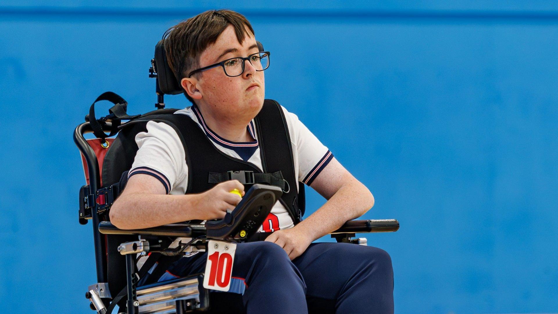 Dan McLellan, a white young man with dark brown hair can be seen in an England shirt using a powerchair