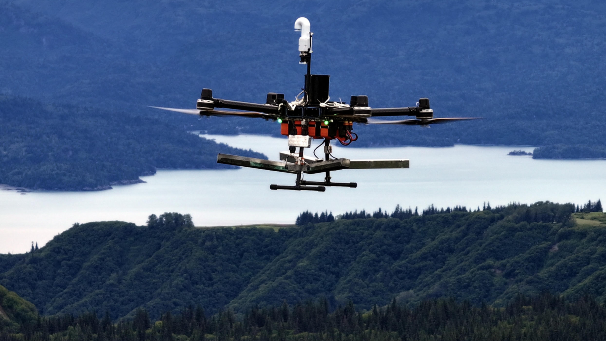A Rainmaker drone flies over forests and a lake in Alaska.