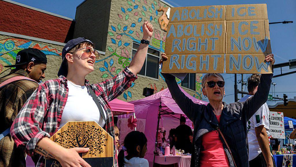 protesters hold up signs, one says "abolish ICE right now" during a parade