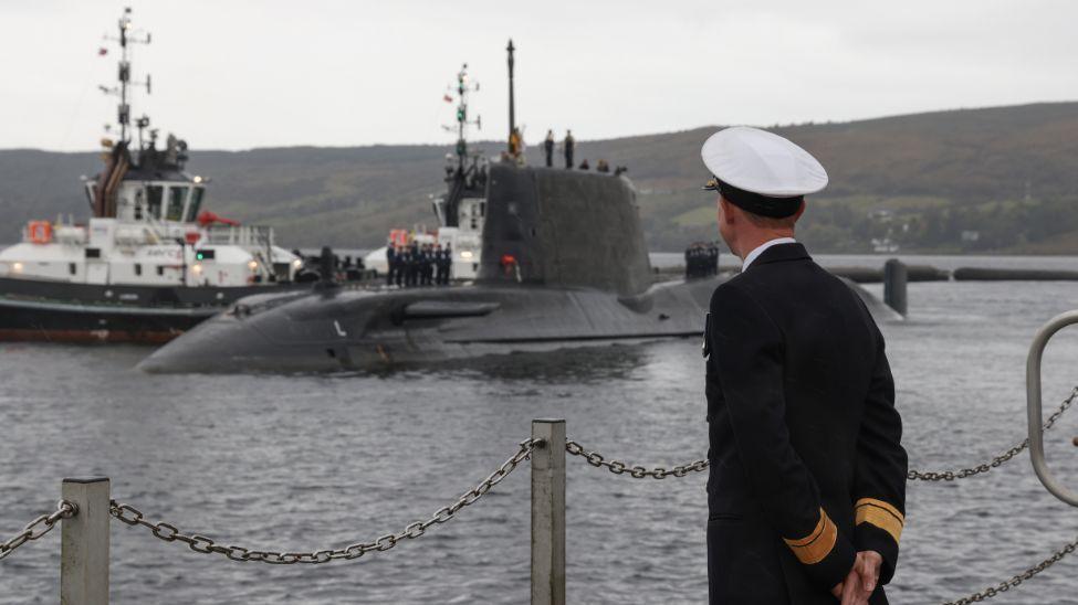 HMS Agamemnon arriving on the River Clyde, watched on by a man in Royal Navy uniform.
