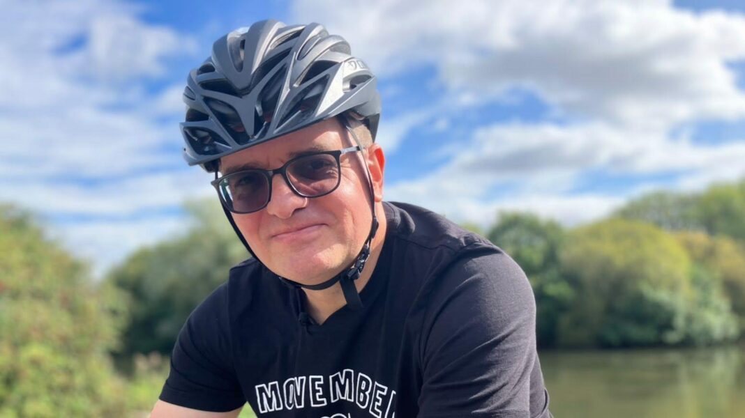 I had to crawl on my hands and knees to get off train, says disabled woman Ben Lidgey is wearing a grey cycling helmet and glasses. He is sat on a bicycle. Ben is wearing a black T-shirt with the visible text “MOVEMBER AMBASSADOR.” Trees and greenery are in the background with a partly cloudy sky.