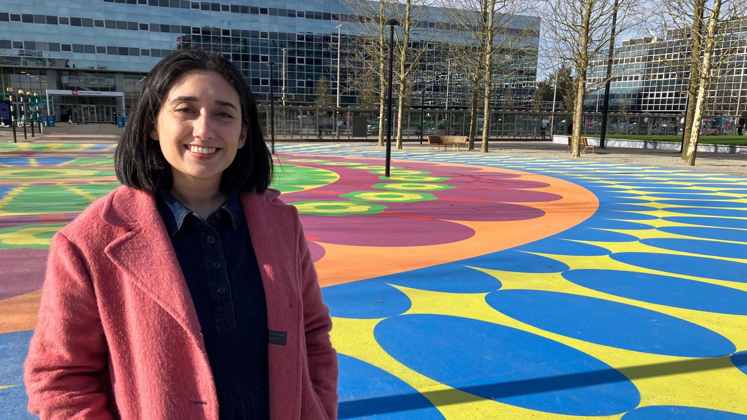 Shanika Mahendran standing in a colourful public square surrounded by modern office buildings.