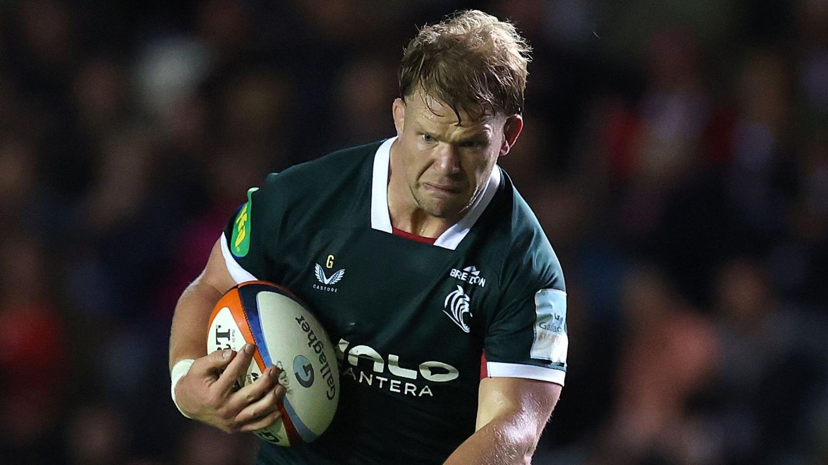Olly Cracknell in green Leicester kit grimaces as he runs with a rugby ball in his left hand