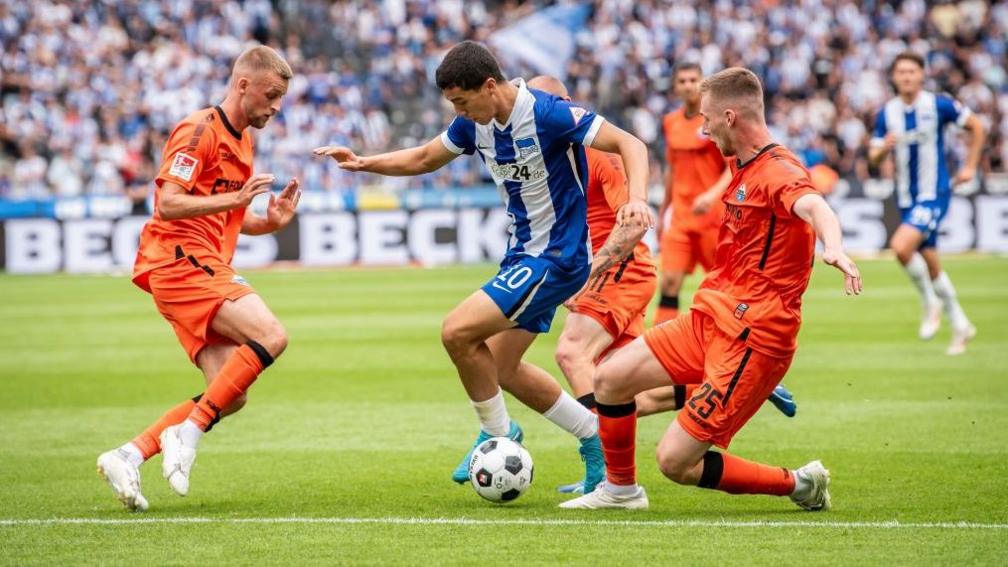 Ibrahim Maza on the ball in Hertha Berlin kit as defenders in orange kit try to stop him