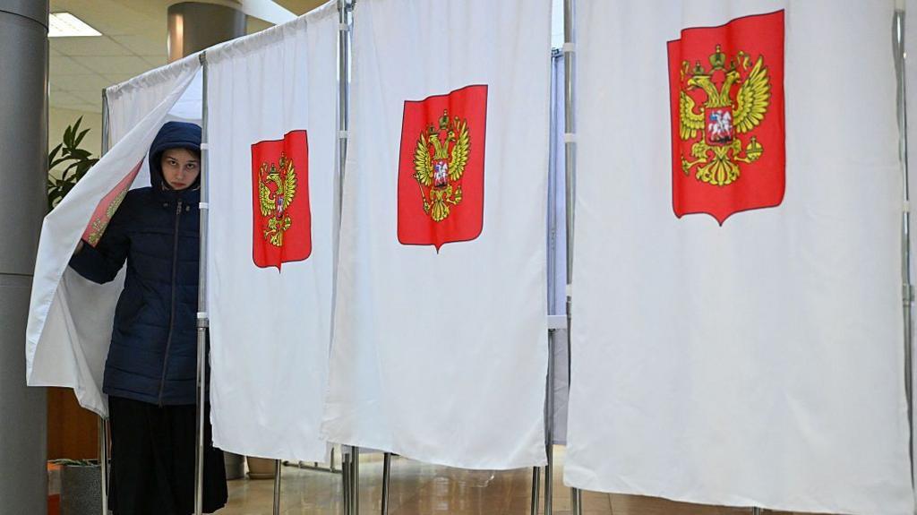 A woman in a dark blue parka leaves a polling booth in Russia