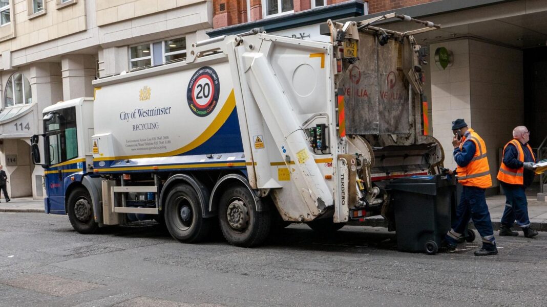 A large white and blue City of Westminster recycling truck parked on a street while two collection workers wearing high-visibility orange vests operate the rear bin mechanism.