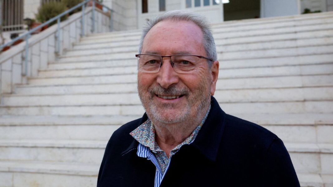 Bernard Baudoux, who has thinning grey hair and glasses, poses for a photograph after he was attacked by Israeli settlers.