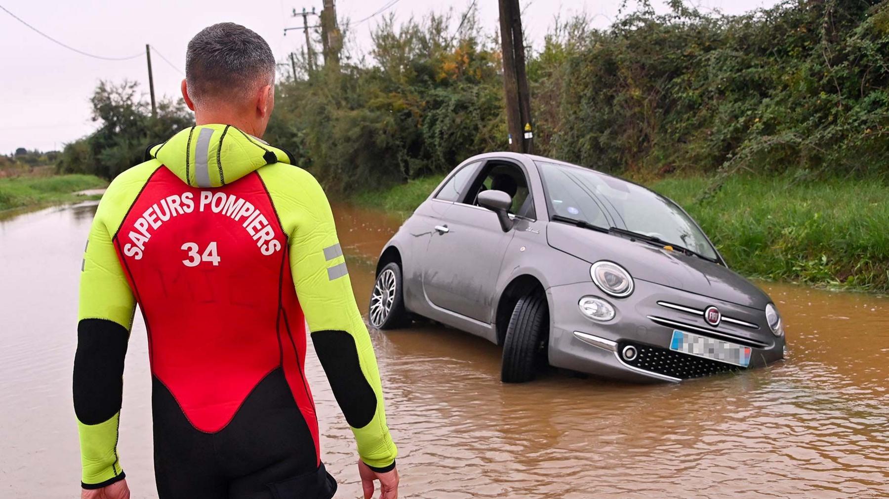 A firefighter checks a damaged car in a flooded street in Lunel, near Montpellier