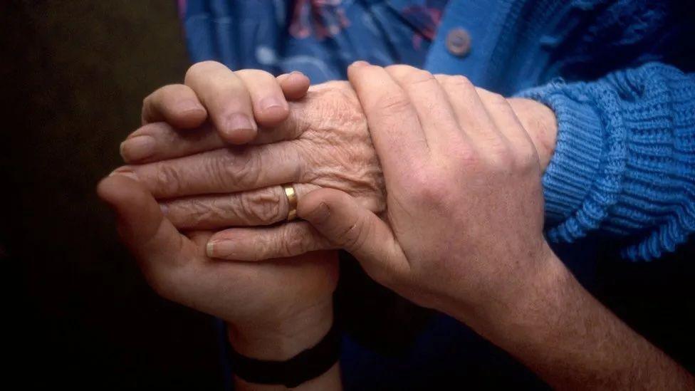 Someone clasps hands around another person's hands, someone wears a blue jumper.