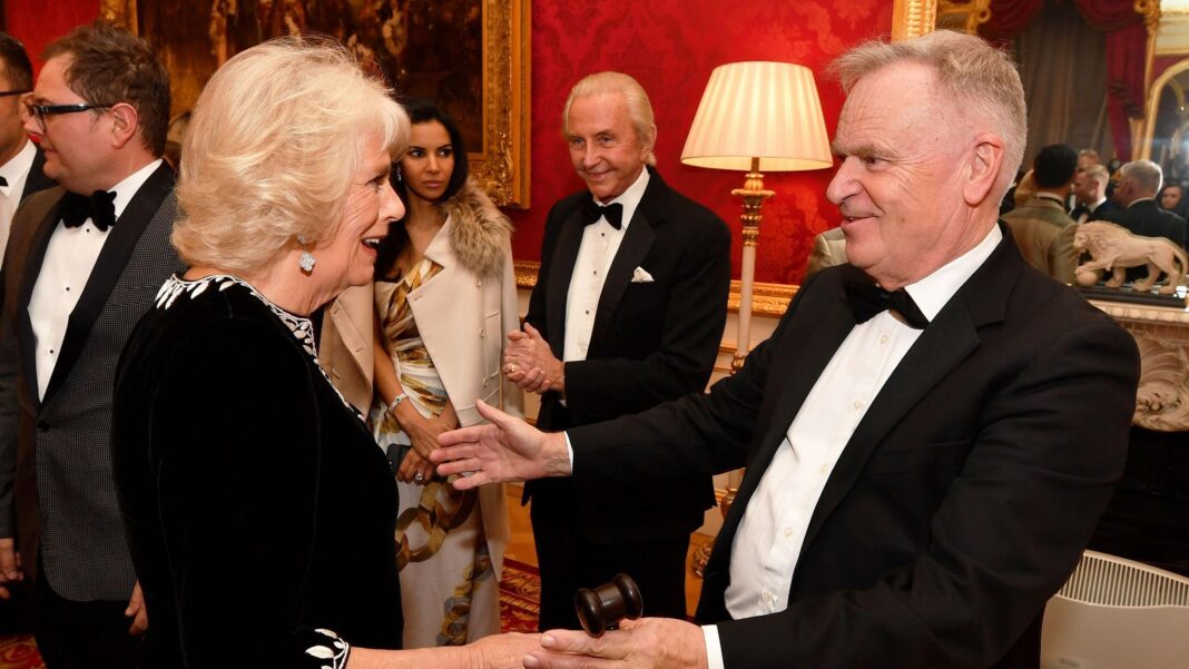Queen Camilla and Jeffrey Archer at a charity reception in 2018. They are greeting each other warmly and both are dressed formally.