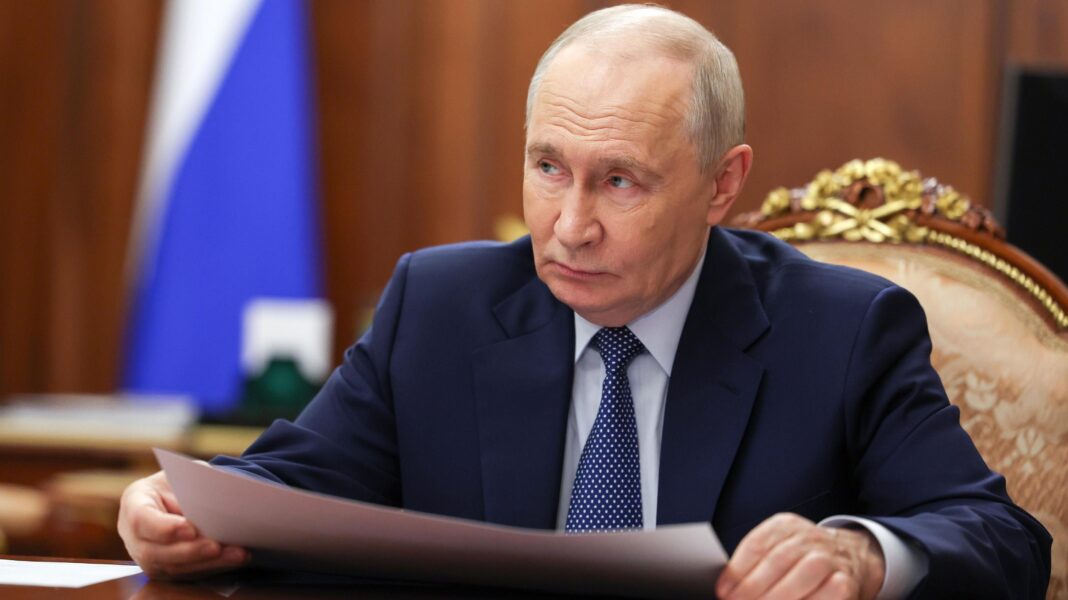 Why Moscow is staying tight-lipped on Trump’s energy ceasefire Russian President Vladimir Putin looks to the side as he sits at a wood table. He is wearing a blue suit and tie and holding a piece of paper