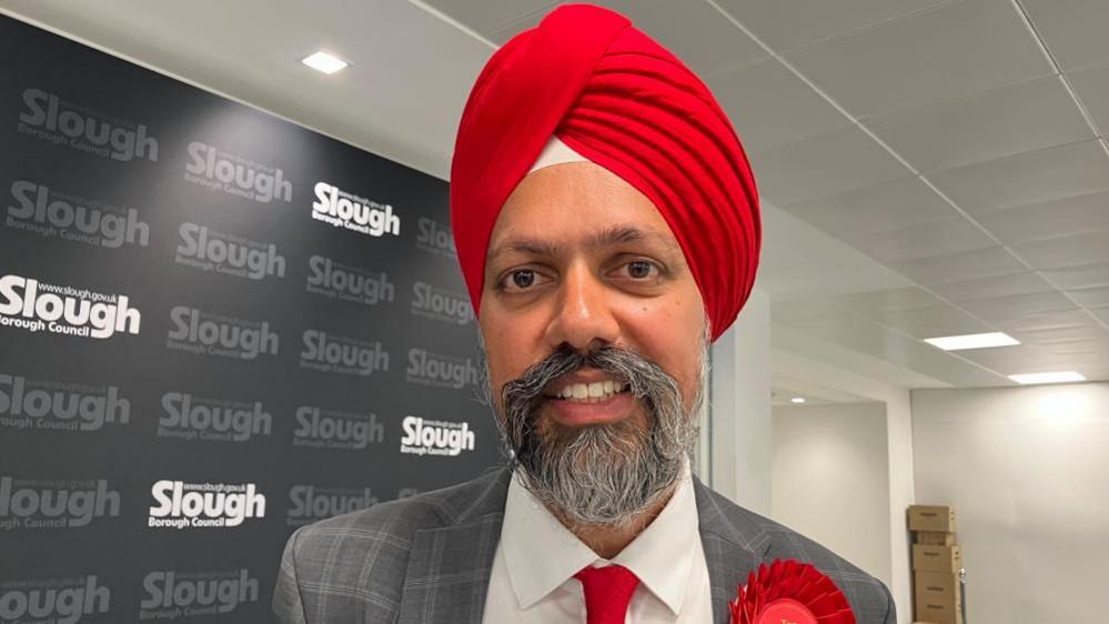 Tan Dhesi smiles while wearing a suit and a red turban.