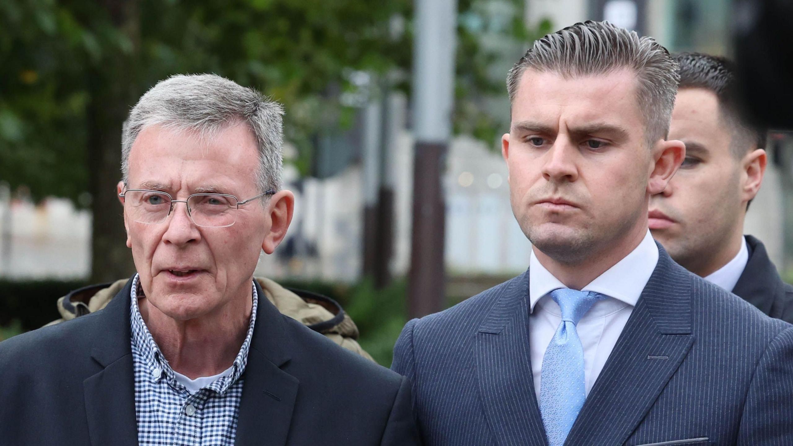 Breandán Mac Cionnaith (left) is wearing a suit with a checkered shirt and Darragh Mackin is wearing a navy suit, a white shirt and light blue tie. They were speaking outside the High Court following the ruling