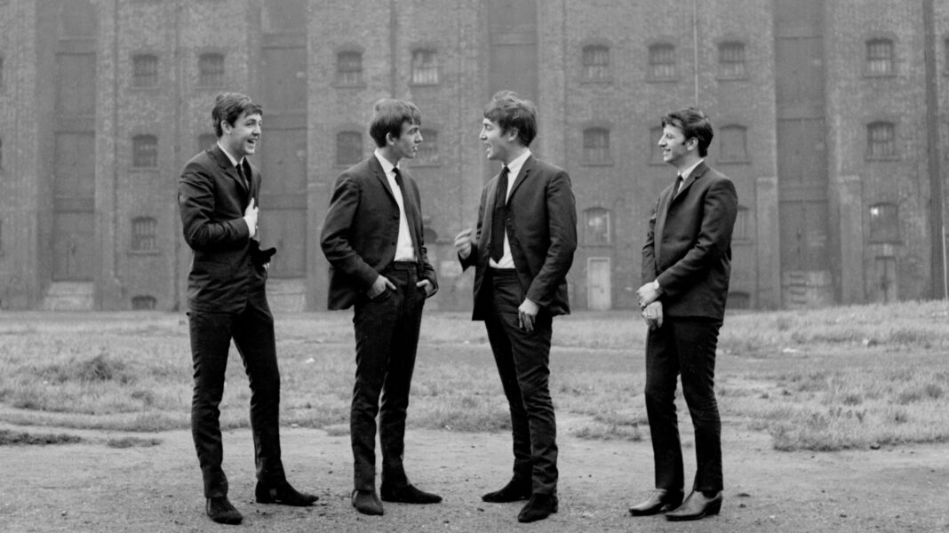 McCartney and Starr back new Beatles attraction Black-and-white image of all four Beatles standing together in front of a large building during the band's early years.