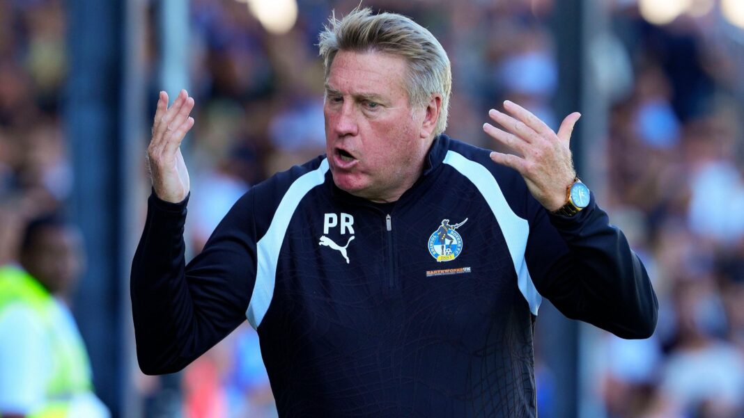 Bristol Rovers coach Raynor diagnosed with bowel cancer Paul Raynor in a dark blue Bristol Rovers tracksuit top urges on the crowd with his two arms raised