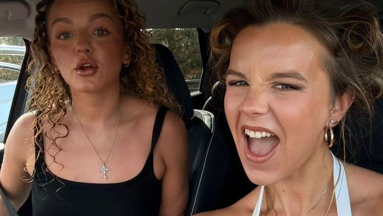 Alex, who has curly blonde hair, and Georgia with brown hair in a bun pull faces in a selfie.