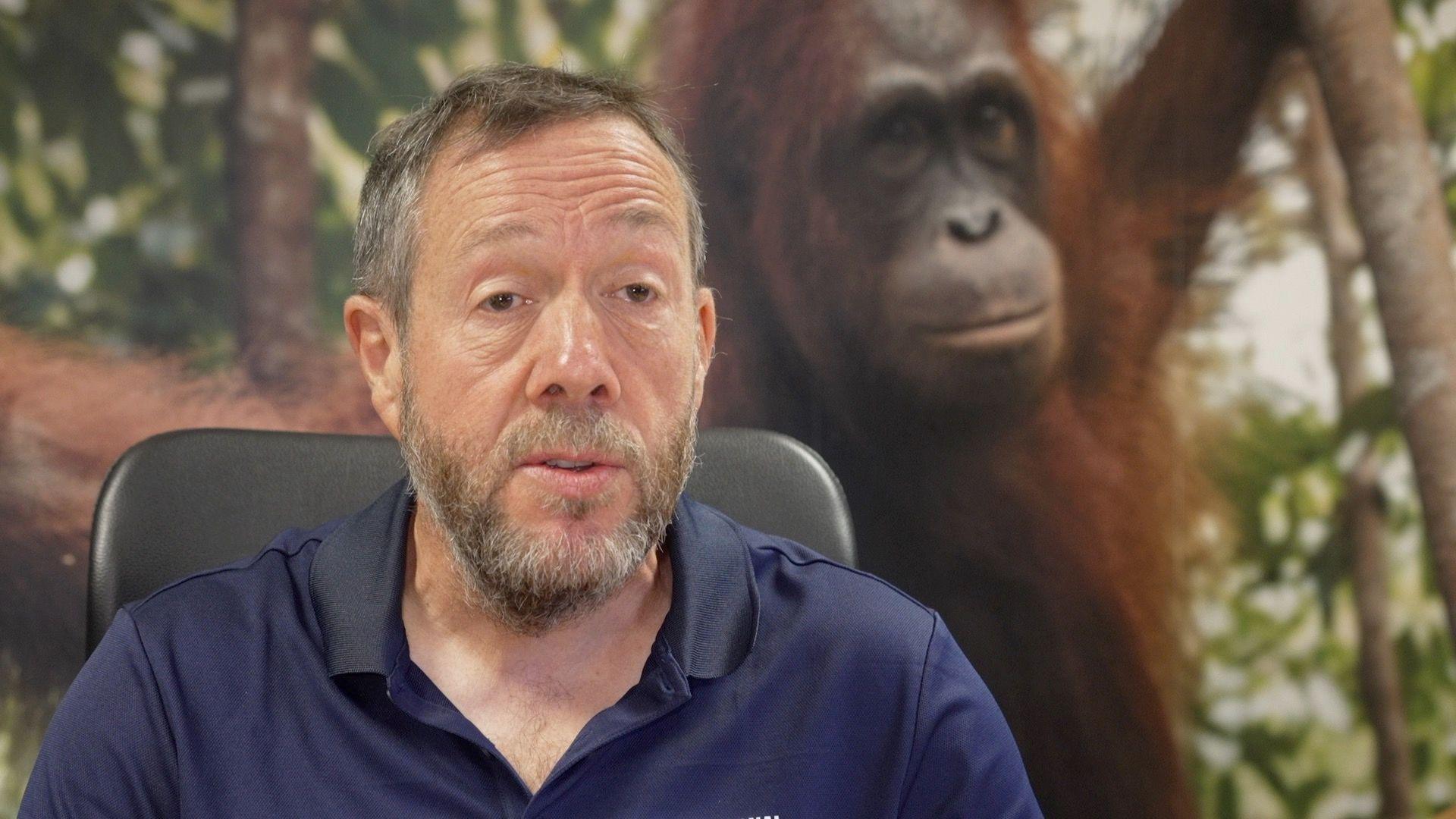 A man in a chair. Behind him is an orangutan.