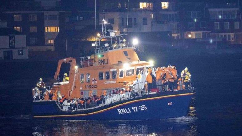 RNLI lifeboat with its decks full of people - the boat is heading in Gosport.  Buildings can be seen in the background.  It is dark/night.