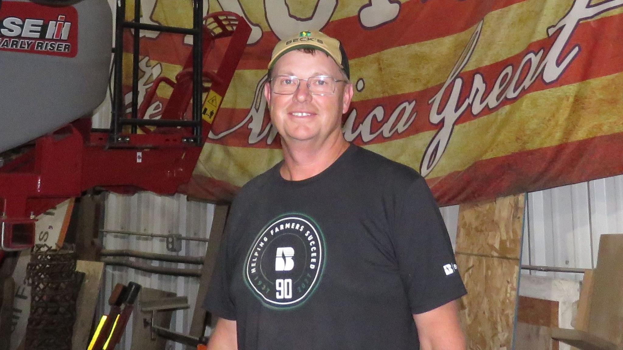Duane Kimball stands in front of farming equipment wearing a hat