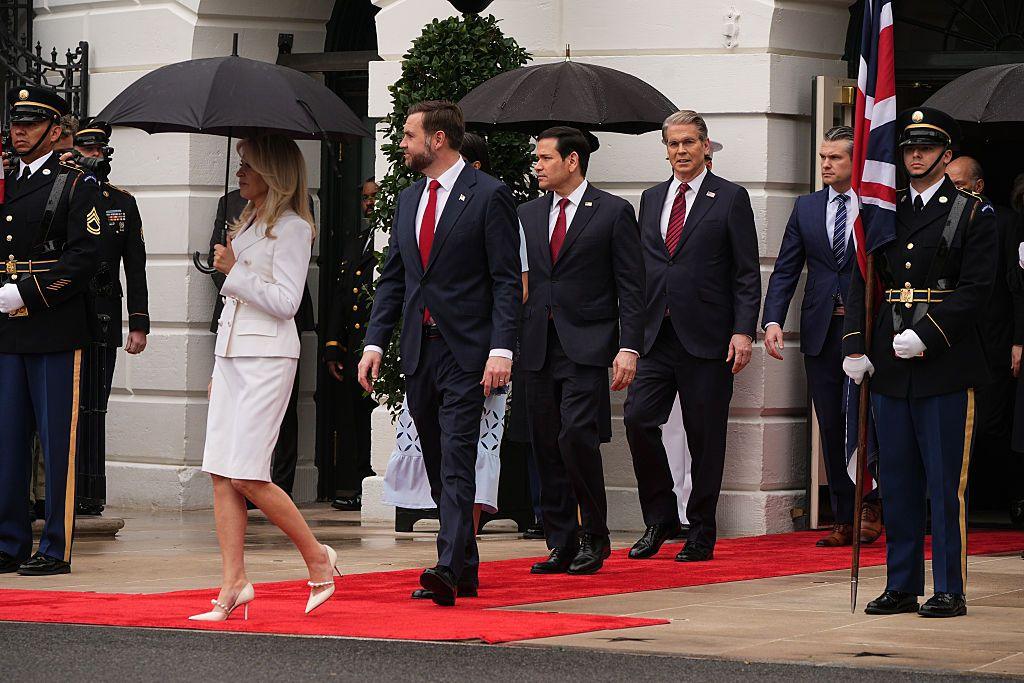 Members of the US cabinet arrive ahead of the ceremonial welcome for King Charles and Queen Camilla on the South Lawn of the White House. A woman in a white skirt suit carries a black umbrella, while (left to right) Vice-President JD Vance, Secretary of State Marco Rubio, Secretary of the Treasury Scott Bessent and Secretary of War Pete Hegseth follow. All are dressed in dark suits with red ties, except for Hegseth who is wearing a striped blue tie.