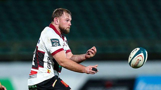 Bryn Robson standing in side profile with his arms going to the right and a rugby ball flying in front of him