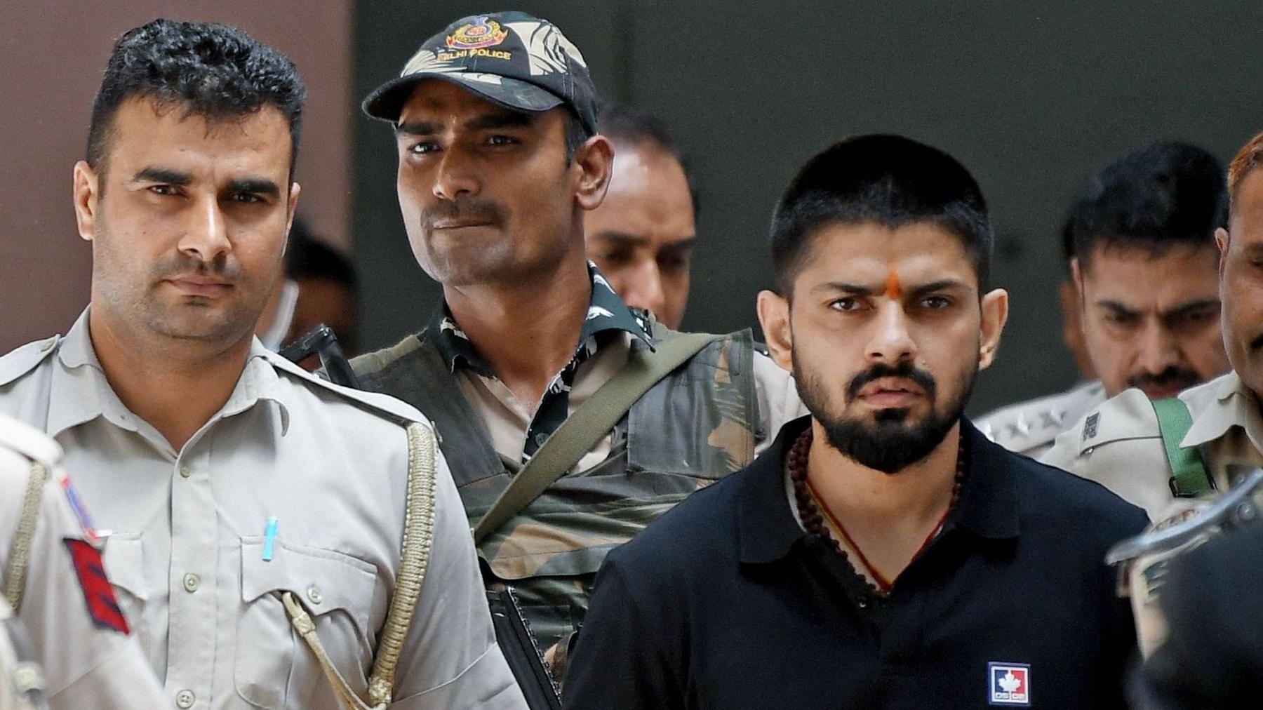 Policemen escort Lawrence Bishnoi at a court, in New Delhi, India on 18 April 2023. He is wearing a black t-shirt and has a tilak (saffron mark) on forehead.