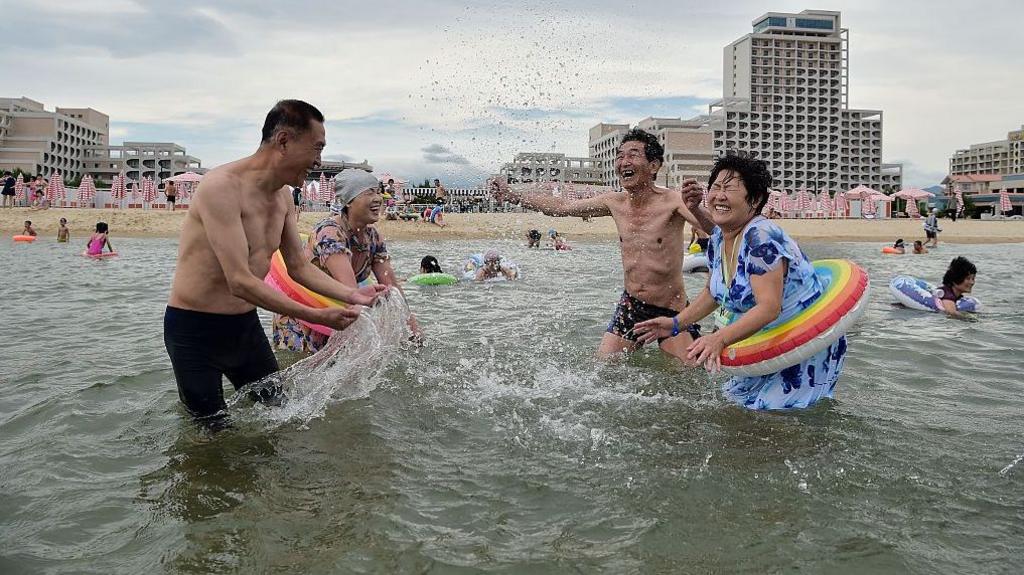 North Korean tourists visit the beach at the Wonsan Kalma Coastal Tourist Area in Wonsan, Kangwon Province, North Korea, on 2 July 2025. Four people in swimsuits splash water at one another.