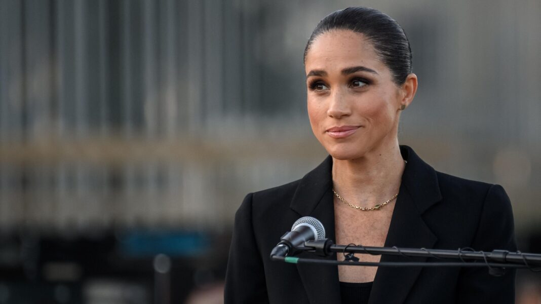 Meghan broke contact with father in letter citing abuse claims Meghan Markle stands behind a microphone wearing a simple charcoal jacket and top, a gold necklace hangs across her chest. Her dark hair is pulled back in a bun.