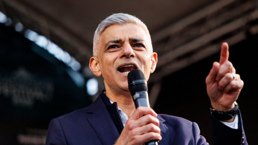 Mayor of London Lord Sadiq Khan speaks on stage. He is wearing a navy jacket and an open-necked white shirt.
